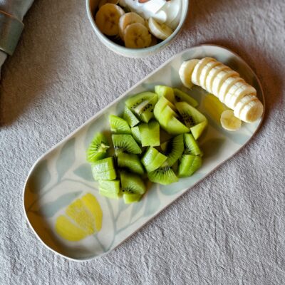 Plat allongé en céramique artisanale décoré avec la technique duy sgraffite, posé sur une table nappée de lin, cotenant des fruits frais, accompagné d'un bol en grès blanc garni de skyr, fruits et amandes